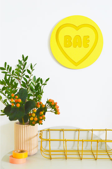 For individuals with visual impairment, 'Bea' is a tactile masterpiece of wall art inspired by classic Love Heart sweets. Dominated by a soothing yellow pastel hue, this piece features a central affectionate message 'Bae,' crafted with elegant gold outlines and additional tactile messages. As a unique addition to our Love collection, 'Bea' serves as a touchable wall decor, adding charm and warmth to your space while brightening the surroundings with love.