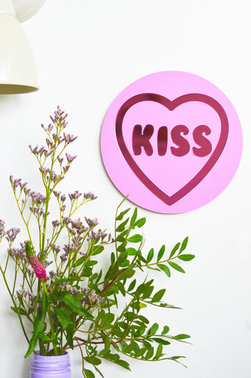 a sweet masterpiece inspired by classic love heart sweets. Featuring a prominent 'Kiss' message and blending pastel lilac color with pink metallic tones, this unique wall decor from our Love Collection is designed to infuse passion and charm into your space, creating a timeless addition that elevates home decor.